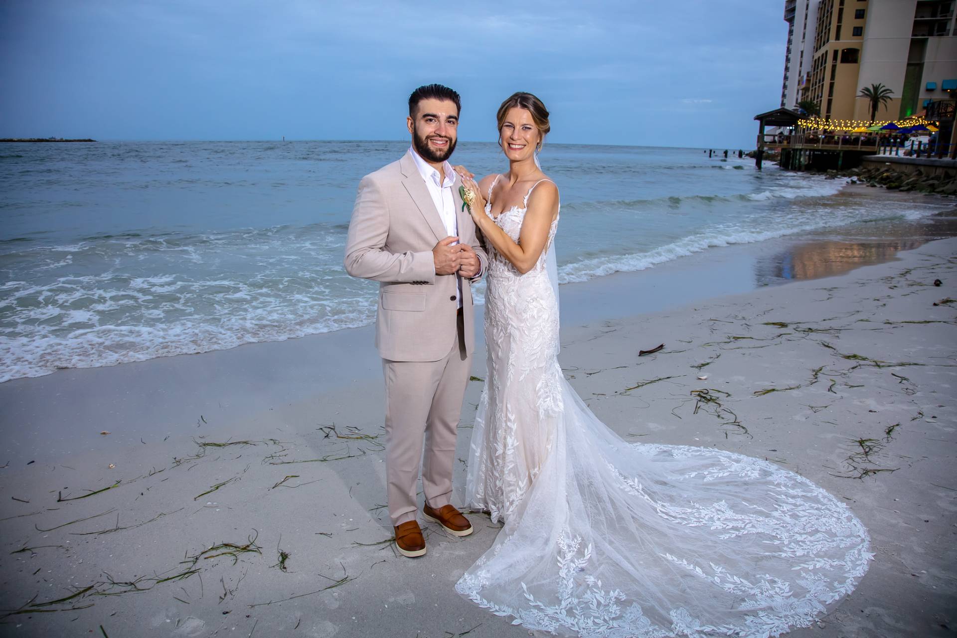 bride hanging out on the grooms shoulder by the water on the beach at sunset