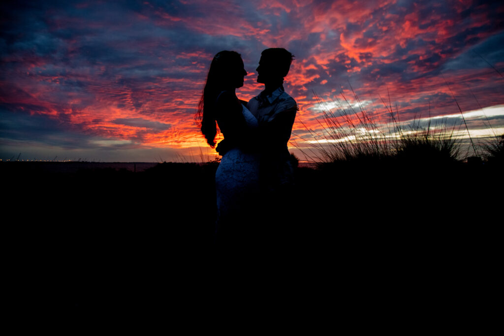 engaged couple holding each other with a fiery sunset