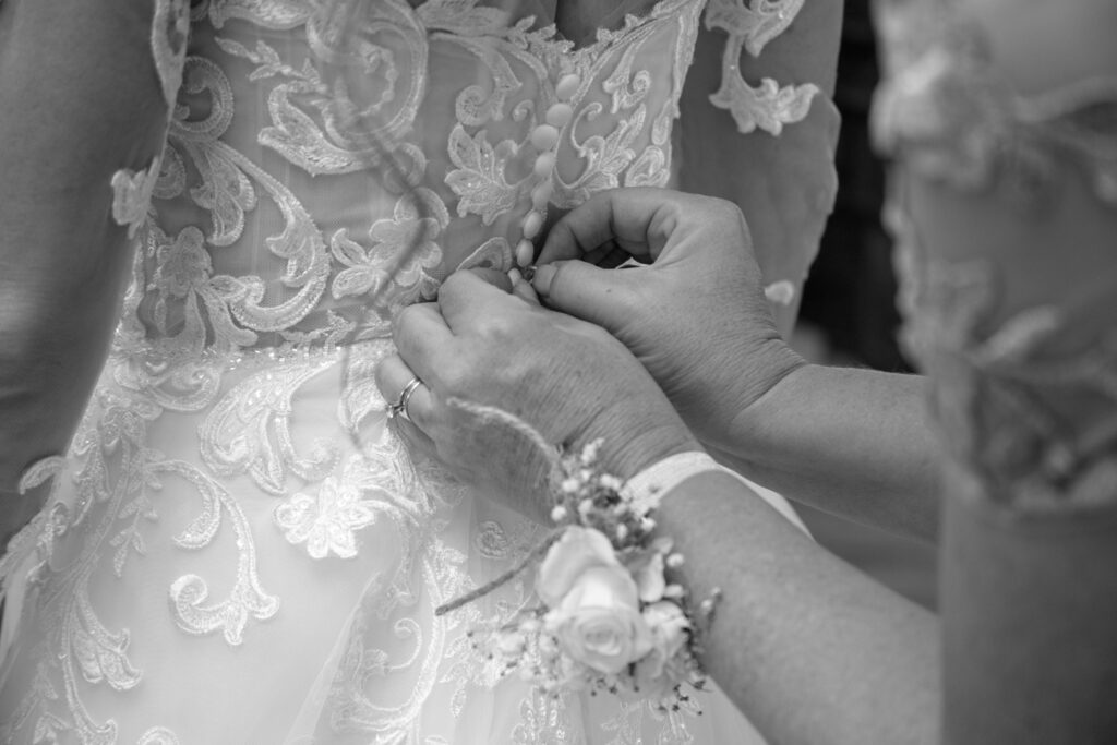 brides mom buttoning up the back of the brides dress