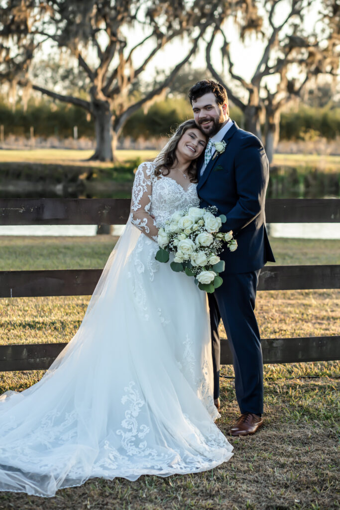 bride resting her head on the groom on front of a wooden fence