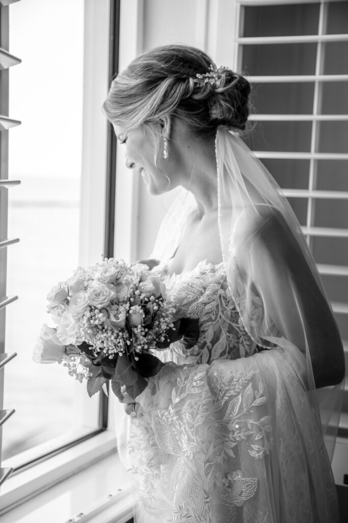 bride looking out the window in her dress with flowers