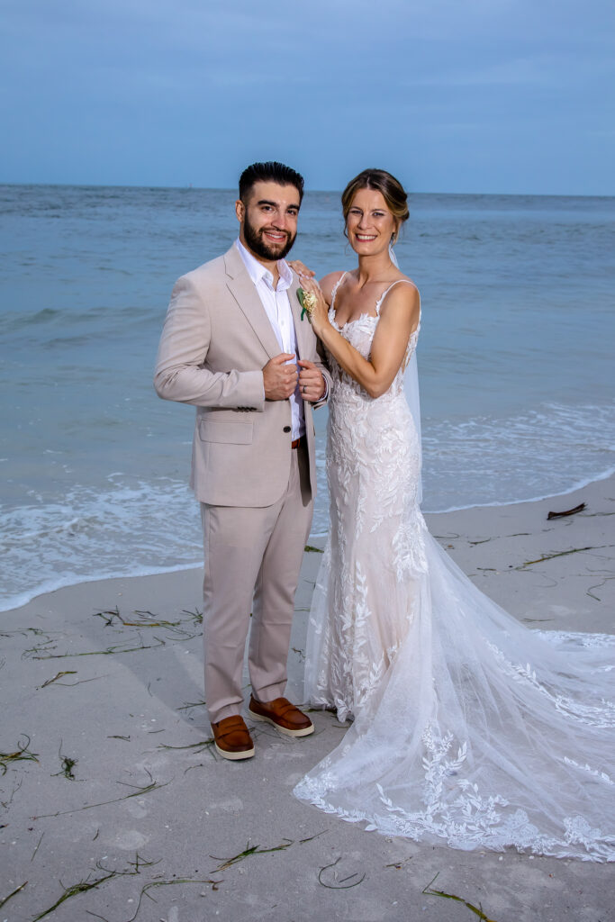 bride hanging out on the grooms shoulder by the water on the beach at sunset
