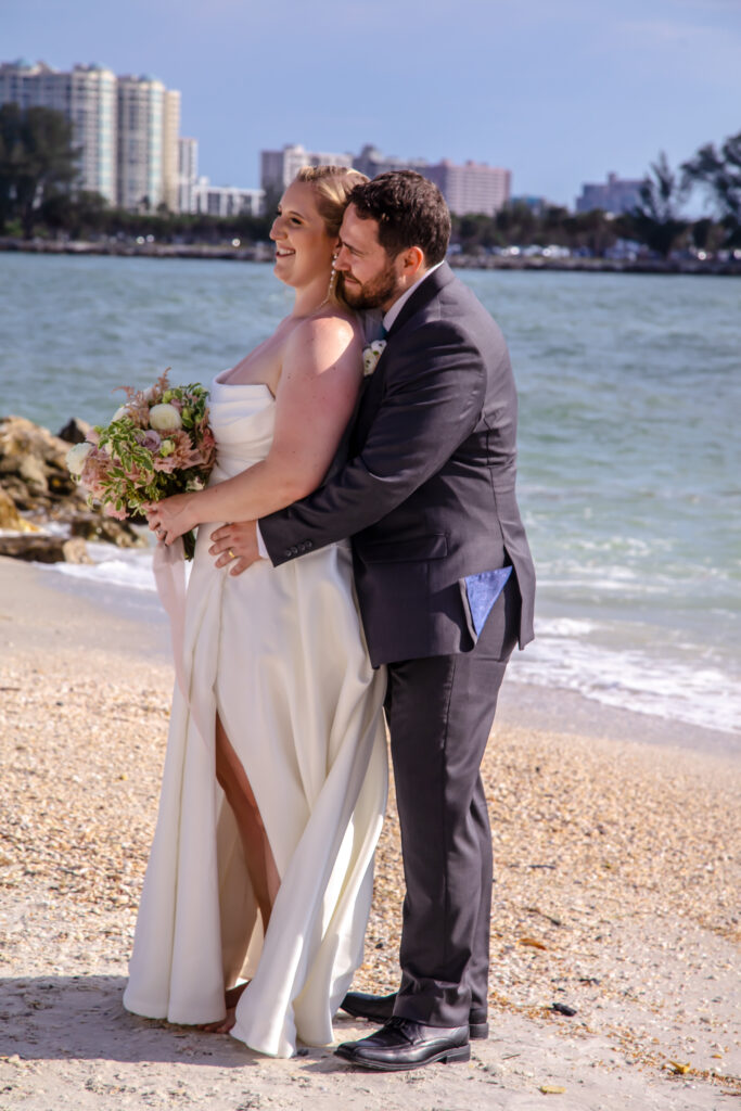 groom holding the bride while they laugh on the beach