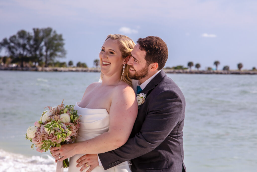 groom holding the bride while they laugh on the beach