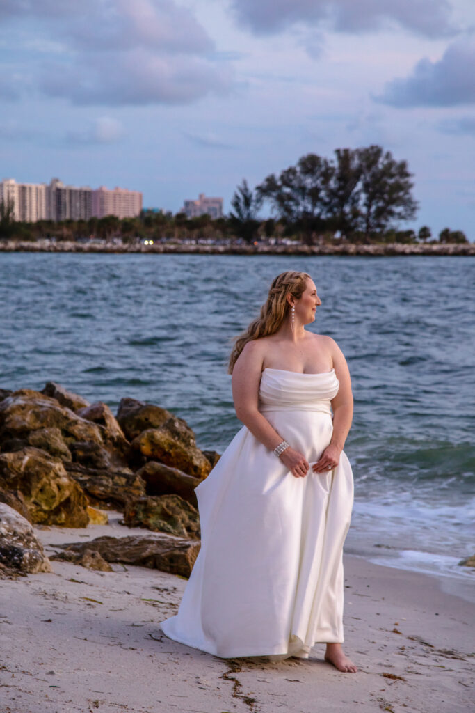bride standing by the waters edge at sunset