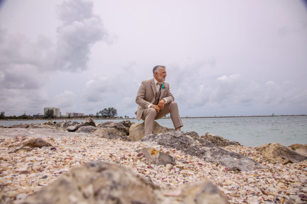 groom sitting on the rocks on the beach