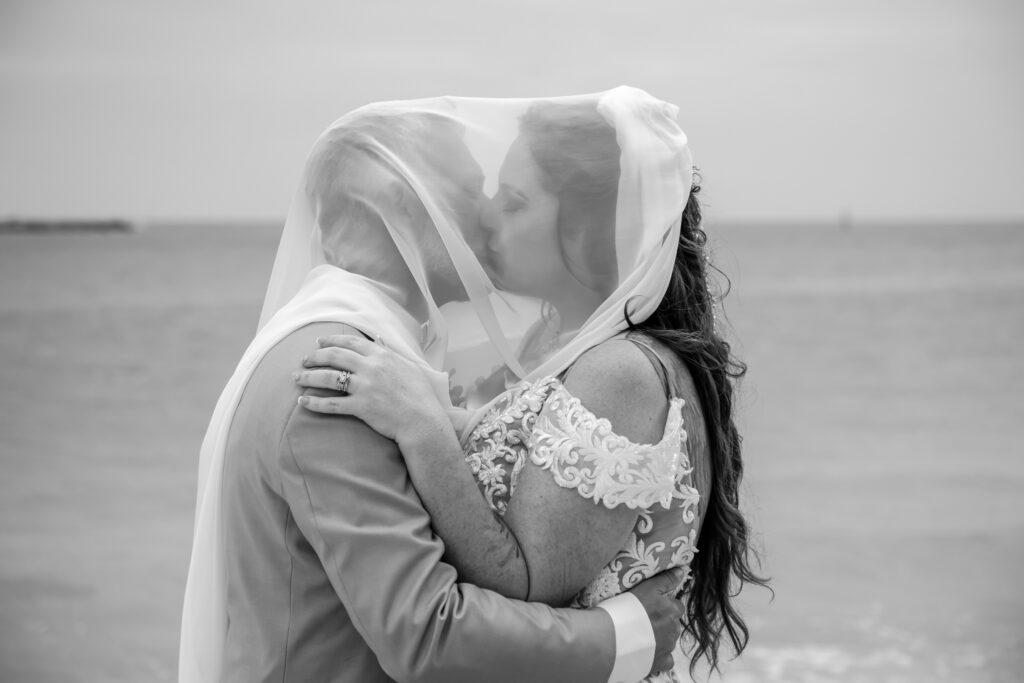 bride and groom under the brides veil, on the beach