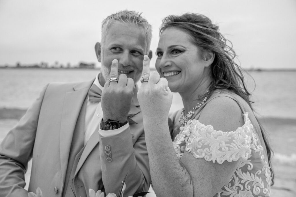 bride and groom flipping their wedding rings fingers to the camera lens