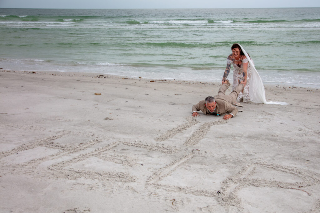 bride dragging groom across the sand
