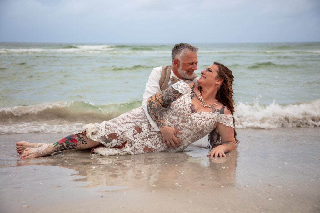 bride and groom laying in the sand on the beach next to waters edge