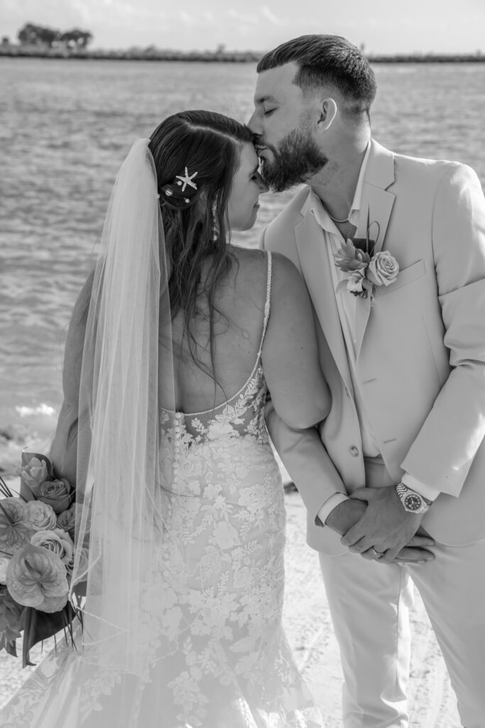 groom kissing the bride on the forehead on the beach