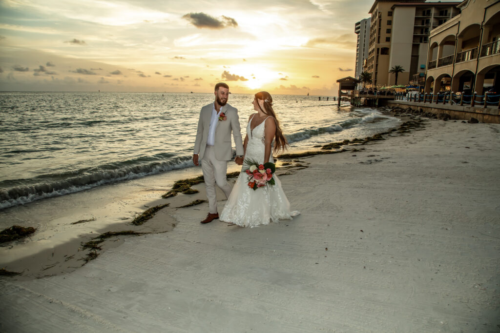 bride and groom walking on the beach at sunset