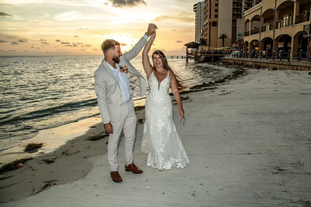 groom spinning the bride around on the beach at sunset